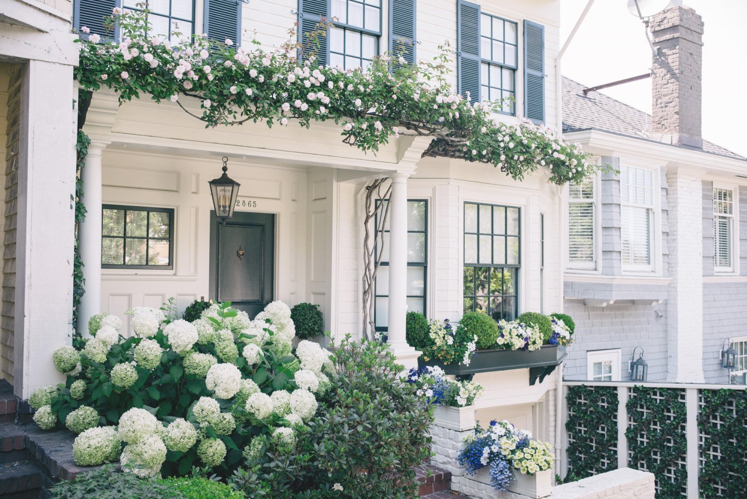 White home with green shutters and lush hydrangeas, representing comfort and simplicity in downsizing.