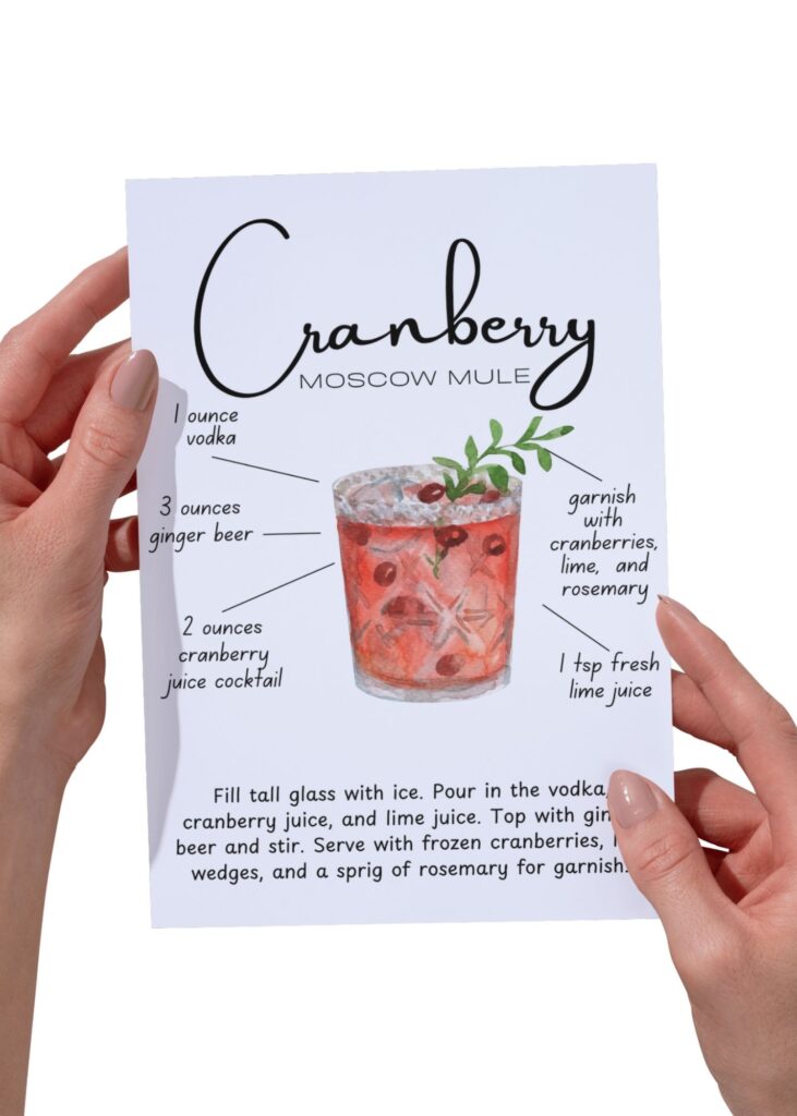 Hands holding a Cranberry Moscow Mule recipe card with ginger beer, vodka, and cranberry juice, garnished with fresh cranberries and rosemary — festive Thanksgiving cocktail.